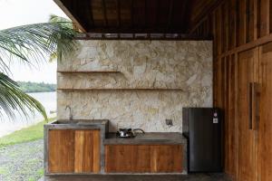 a kitchen with a sink and a refrigerator next to a stone wall at Cay's House Batukaras in Batukaras