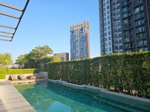 a swimming pool in front of a hedge with buildings at Urbitia Thonglor in Klong Toi
