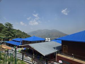 a building with blue roofs with mountains in the background at devdaar hills homes cafe & resort in Mussoorie