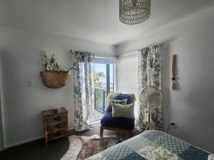 a bedroom with a bed and a chair and a window at Darlene's Nest in Cable Bay