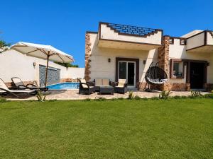 a house with an umbrella and chairs and a pool at Nubian Villa with Private Pool in Naj‘ al Aḩwāl