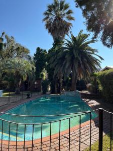 a swimming pool with palm trees and a fence at Gemstone Guest House in Klerksdorp