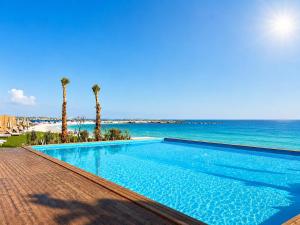 a swimming pool next to the ocean with palm trees at XU Sidi Abdel Rahman Resort & Spa in El Alamein