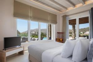 a bedroom with a bed with a television and windows at Andros Royal Villa in Koumárion