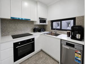 a kitchen with white cabinets and a sink at Matildas Urban Escape 6-Min Station & Shops in Campbelltown South
