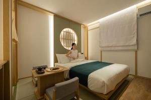 a woman sitting on a bed in a room at Anook Ryokan Hotel Suwon Ingye in Suwon