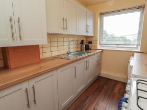 a kitchen with white cabinets and a sink and a window at Flodden Apartment in Wooler