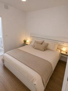 a white bedroom with a large bed with two lamps at Estudio a 300 mts de la playa in Puebla de Farnals