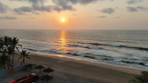 a sunset over the ocean with umbrellas on the beach at La Parshwa Villa Maré in Mahabalipuram