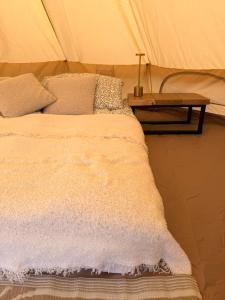 a bed with a white blanket and a table at Glamping Fit in the wild in Forest Row