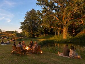 a group of people sitting around a fire near a pond at Glamping Fit in the wild in Forest Row