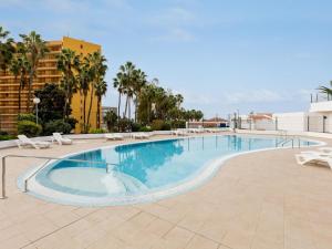 a large swimming pool with white chairs and palm trees at Cute Las Flores 1i with pool in Costa de Adeje