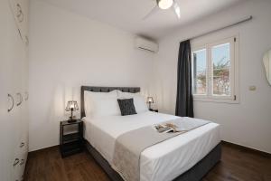 a white bedroom with a large bed and a window at Passa Corda Villa in Agios Prokopios