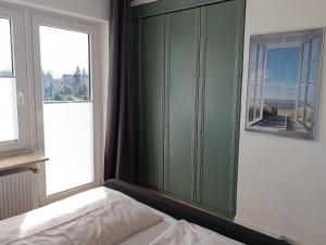a bedroom with a green cabinet and two windows at Haus Schildt, FeWo 3 in Duhnen