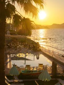 ein Pool mit Tischen und Stühlen und das Meer bei Sonnenuntergang in der Unterkunft Agoulos Beach Hotel in Argassi