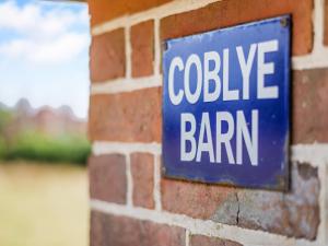 a blue sign on a brick wall with the words college barn at Coblye Barn in Battle