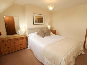 a bedroom with a white bed with a dresser and a mirror at Sarah's Cottage in Berwick-Upon-Tweed