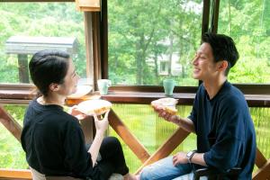 a man and woman eating hot dogs in front of a window at コテージひだまり in Izunokuni