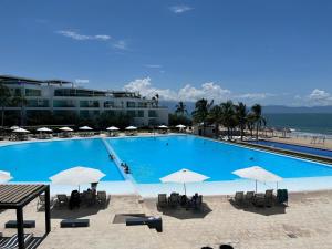 a large swimming pool with umbrellas and the ocean at Aria Ocean Rentals - Riviera Nayarit in Nuevo Vallarta