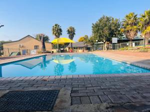 a swimming pool with a yellow umbrella and palm trees at Pendleberry Unit 85 in Warmbaths