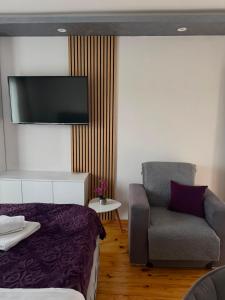 a bedroom with a bed and a chair and a flat screen tv at Apartman Ena in Nova Varoš