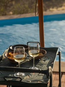 two glasses of white wine on a table next to a pool at Boscia African Farm in Omomas +41 photos