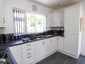 a kitchen with white cabinets and a sink and a window at Ger y Mynydd, 2 Cae Ty Coch in Brynteg