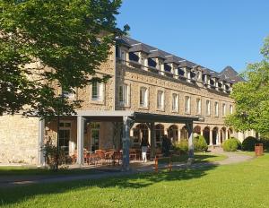 a large brick building with tables and chairs at LOGIS HOTEL L'HÔTEL DES BAINS - Salles-la-Source in Salles-la-Source