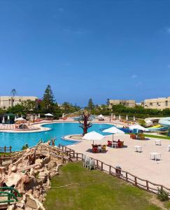 a swimming pool with tables and umbrellas at a resort at Charming 3BDR Chalet l North Coast in Dawwār Muşādif Yūnus