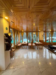 a large room with wooden ceilings and tables and windows at Gaunnie Valley - Jibhi in Jibhi