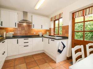 a kitchen with white cabinets and a sink and windows at Willow Cottage in North Lydbury