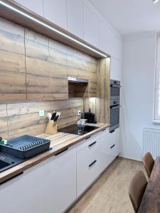 a kitchen with white cabinets and a wooden wall at Sarah Doe Apartman in Nyíregyháza