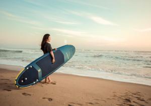 a woman standing on the beach holding a surfboard at De Waves Varkala by VOYE HOMES - Just 1 Km from Varkala Cliff and Beach in Varkala
