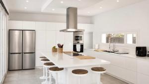 a white kitchen with a white counter and stools at Villa Guvalmar Chalet Roche in Roche