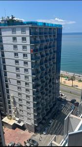 a tall building with cars parked in front of the ocean at 2 минуты до моря in Batumi