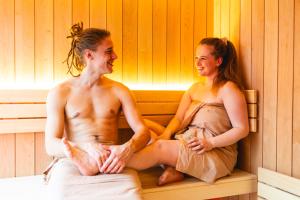 a man and a woman sitting in a sauna at El Nido wellness a spa in Vysoké Mýto