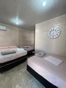 three beds in a room with a clock on the wall at Pousada Neca Raabe in Pântano Grande