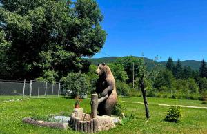 a bear statue sitting on a stump in a yard at Белите Къщи in Seltse
