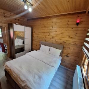 a bedroom with a white bed in a wooden wall at Katipogulları Apart in Uzungöl