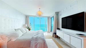 a white bedroom with a large television and a bed at Jade Beach Escape in Sunny Isles Beach