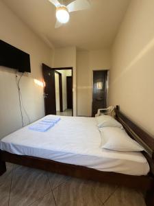 a bedroom with a bed with white sheets and a television at Pousada Flor do Vale in São José dos Campos