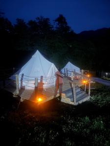 two large white tents are lit up at night at Vatra Bunătăților- By The Lake in Proeni