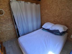 a small bed with two pillows and a curtain at Refuge climatisé tout proche du Pal in Le Pin