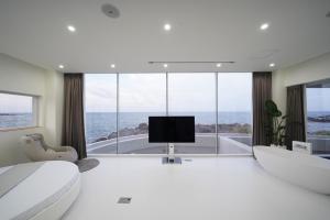 a white bedroom with a television and large windows at Pohang Horizon Poolvilla in Pohang