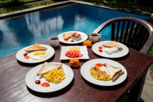 four plates of breakfast foods on a table near a pool at Ayu Shanti Guest House Ubud in Ubud