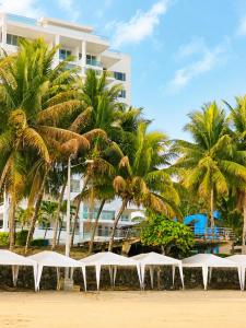 a row of white tables on a beach with palm trees at Playa Azul Exclusive Suites in Tonsupa
