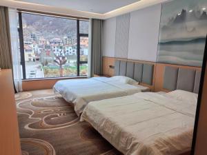 two beds in a hotel room with a large window at 四川思睿博酒店 in Heishui