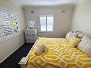 a bedroom with a yellow and white bed and windows at Our Place in South West Rocks