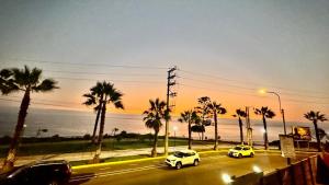 three cars driving down a street with palm trees at Hotel Sunset Mar in Lima