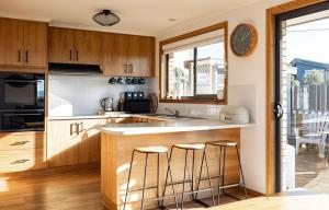 a kitchen with wooden cabinets and a counter with stools at Drift - Watch the world go by in Scamander